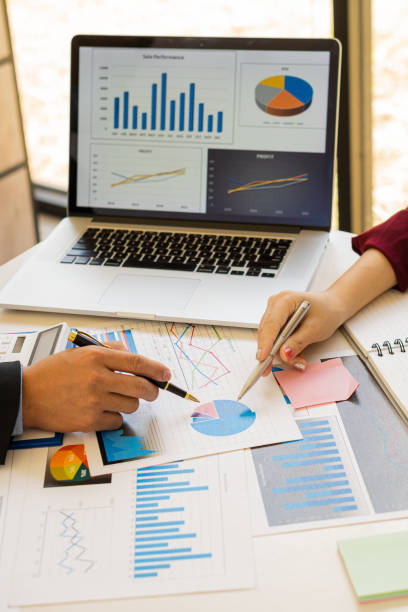 Businessman holding a pen pointing to analyze paper financial graph on the table and investment planning for businesses and accountants working using a calculator with a vertical picture laptop. hombre de negocios sosteniendo un bolígrafo apuntando para analizar el gráfico financiero de papel sobre la mesa y la planificación de inversiones para empresas y contadores que trabajan utilizando una calculadora con una computadora portátil de imagen