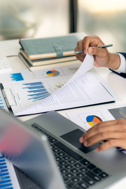 Businessman holding a pen pointing to analyze paper financial graph on the table and investment planning for businesses and accountants working using a calculator with a vertical picture laptop. hombre de negocios sosteniendo un bolígrafo apuntando para analizar el gráfico financiero de papel sobre la mesa y la planificación de inversiones para empresas y contadores que trabajan utilizando una calculadora con una computadora portátil de imagen