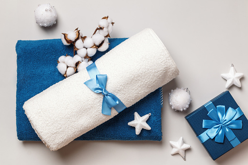 White and blue terry towels with a bow on a gray background. Gift box cotton branch with Christmas decorations.