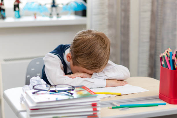 istock A cute first grader boy in a school uniform at home during a pandemic fell asleep doing homework at a desk with books and pencils. Selective focus. Close-up 1357444334