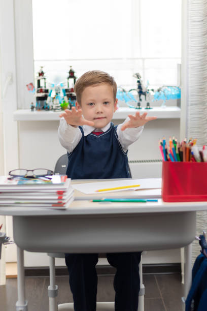 istock Cute boy first grader in school uniform at home during a break fooling around while sitting at his desk. Selective focus. Close-up 1357444339