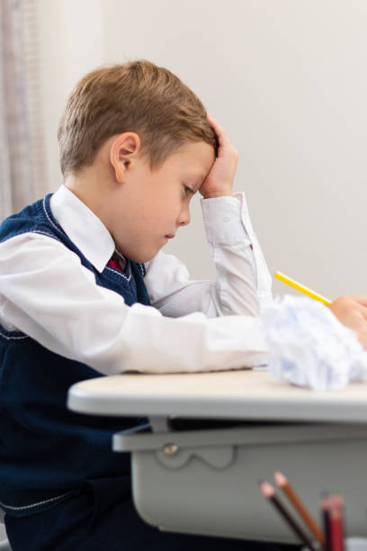 istock A cute boy first grader in a school uniform does homework while sitting at a desk with a pencil in his hands at home. Remote education. Selective focus. Close-up 1357444341