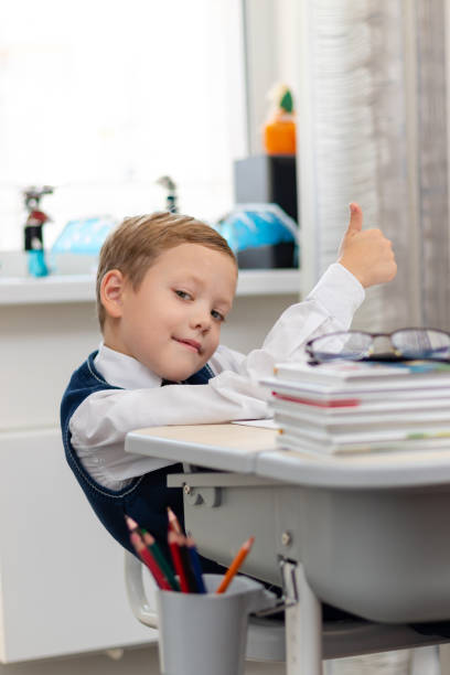istock Cute boy first grader in school uniform at home during a break fooling around while sitting at his desk. Selective focus. Close-up 1357444367