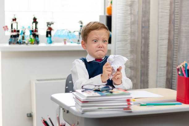 istock Cute boy first grader in school uniform at home during a break fooling around while sitting at his desk. Selective focus. Close-up 1357444379