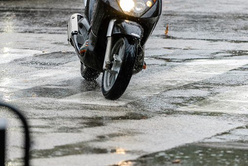Detail of a motor scooter crossing the road in pouring rain.
