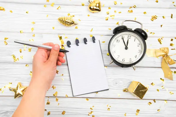 Festivedecorations and notebook with wish list and alarm  on white rustic table, flat lay style. Planning concept.