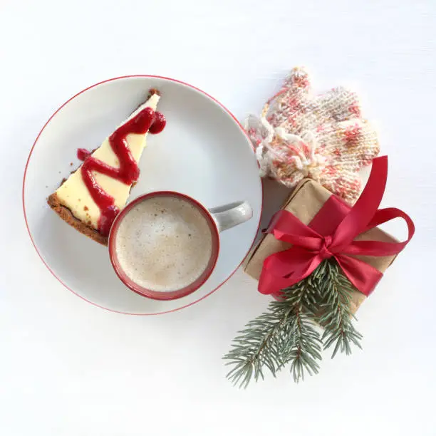 slice of cheesecake and a gift decorated with a spruce branch with a cup of frothy cappuccino top view