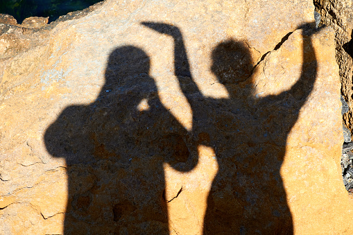 The shadow of a married couple being photographed against the backdrop of a rock on a bright sunny day.