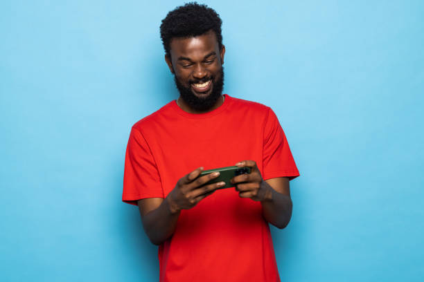 istock Young african american man Play game with mobile phone posing isolated on blue background. People lifestyle concept. 1357457366