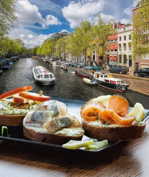 Amsterdam city with fishplate (salomon and codfish sandwiches) against tourboat on canal in Netherlands