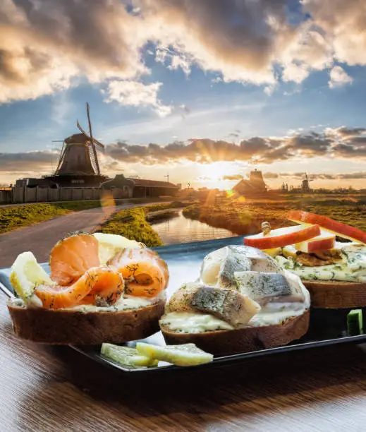 Traditional Dutch windmills with fishplate( salomon and cod sandwiches) against sunset in Zaanse Schans, Amsterdam area, Netherlands