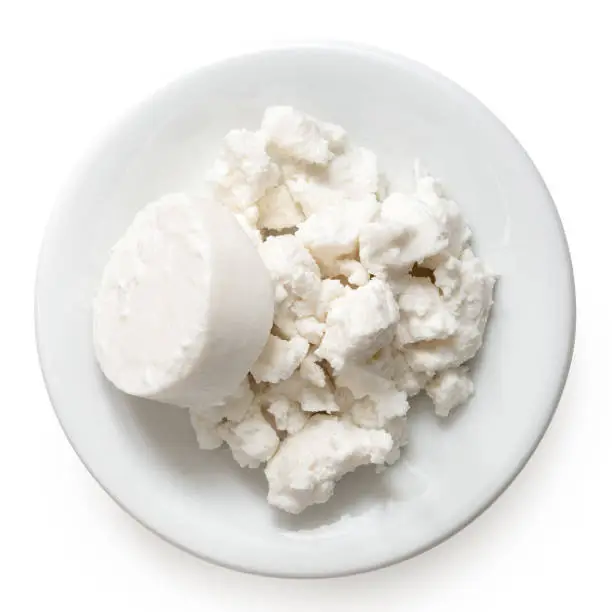 Round of goat cheese and crumbled goat cheese on white ceramic plate isolated on white. Top view.