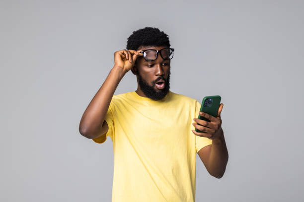 istock Surprise. Shocked young African man using smart phone while standing isolated grey background 1357460224
