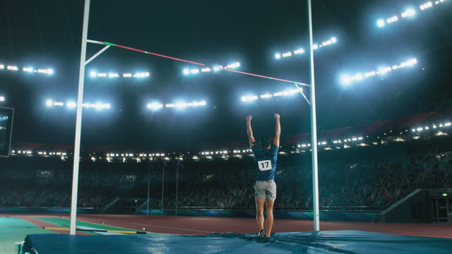 Pole Vault Jumping Championship: Professional Male Athlete Running with Pole Successfully Jumping over Bar and Landing on His Feet, Celebrates Record Setting Victory with Stadium Crowd Cheering