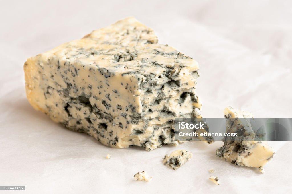 Blue cheese. Broken blue cheese wedge with crumbles on wax paper.. Crumble - Dessert Stock Photo