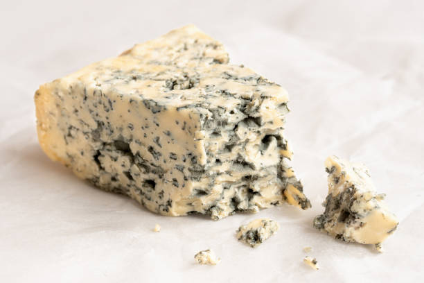 Blue cheese. Broken blue cheese wedge with crumbles on wax paper.. blue cheese stock pictures, royalty-free photos & images
