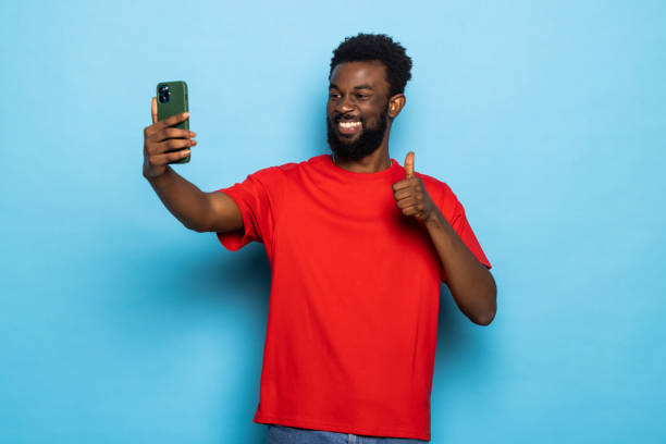 istock African man making selfie gesturing thumbs up posing over blue background. 1357460971