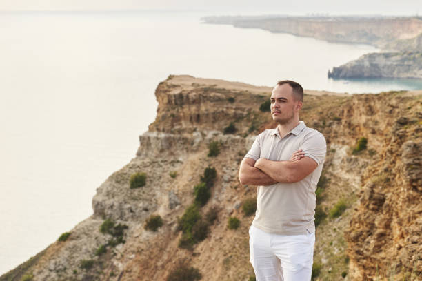 istock young handsome serious man standing on a rocky seashore with his arms folded on his chest 1357461175