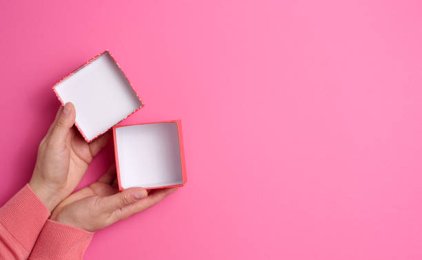 istock female hands holding open square cardboard gift box on pink background, top view 1357461190