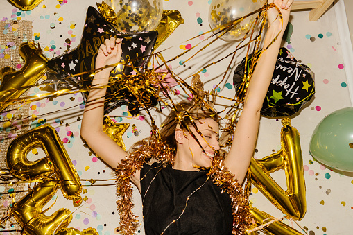 Photo of a young woman lying down on the floor, tangled in decoration after the New Year's Eve party