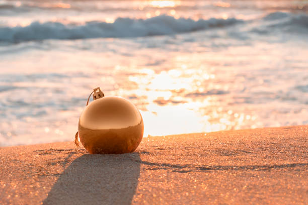 christmas golden ball on seashore sand. blurred sea wave in background. christmas and new year at beach concept. greeting card. selective focus, copy space - christmas beach sun tropical climate imagens e fotografias de stock