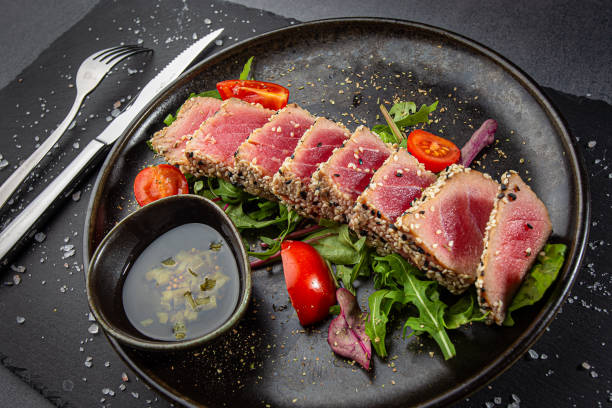 zbliżenie plasterków tuńczyka zsieki sezamu i świeże warzywa na ciemnym talerzu. - arugula cooked spice lettuce zdjęcia i obrazy z banku zdjęć