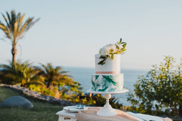 Elegant wedding cake with two tiers decorated with white flowers and placed on table on blurred background of sea and blue sky