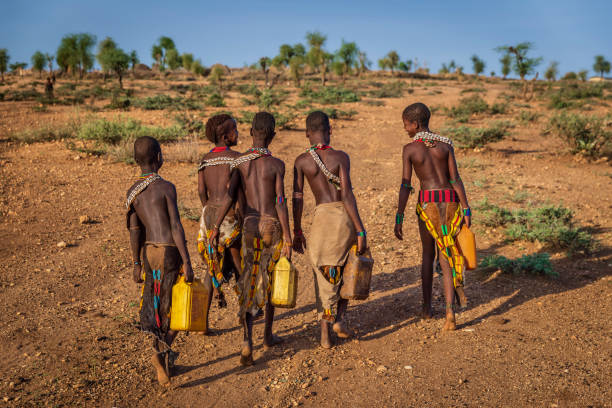 afrikanische mädchen, die wasser aus dem brunnen tragen, äthiopien, afrika - hamer woman stock-fotos und bilder