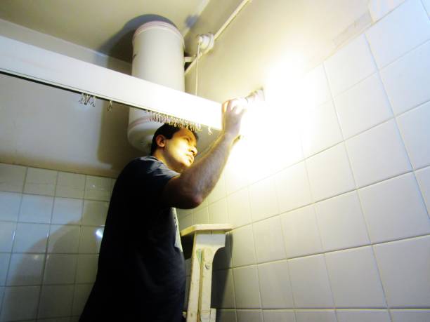 Bathroom Fittings A young man fixing the lights and other electrical equipment in the bathroom. bathroom geyser stock pictures, royalty-free photos & images