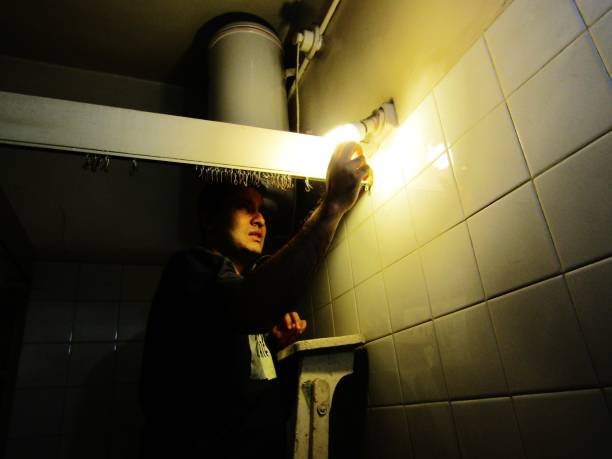 Bathroom Fittings A young man fixing the lights and other electrical equipment in the bathroom. bathroom geyser stock pictures, royalty-free photos & images