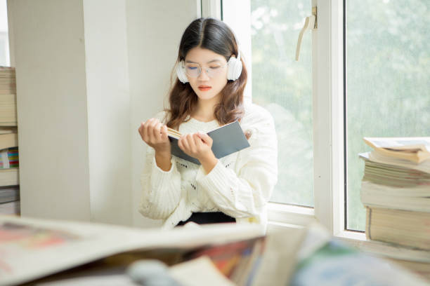istock Women, windows, headphones, reading, learning, education 1357471272