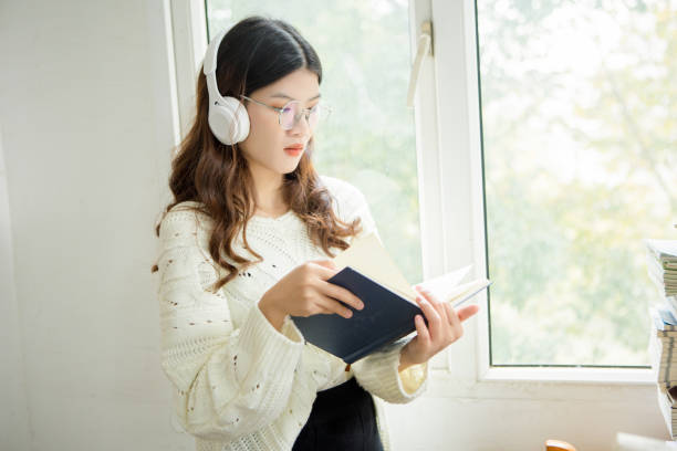 istock Women, windows, headphones, reading, learning, education 1357471300