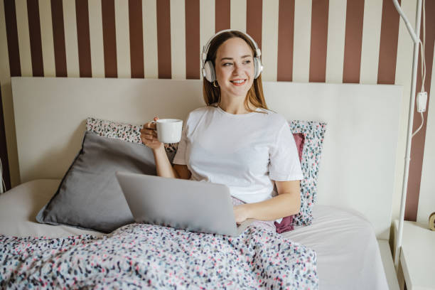 istock Young woman drinking morning coffee in bed and using laptop 1357472819