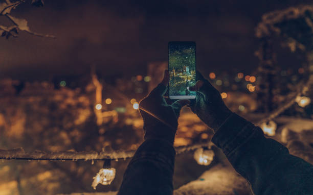 Photo of a man holding his phone and taking pictures of the first snow in his city, from a balcony.