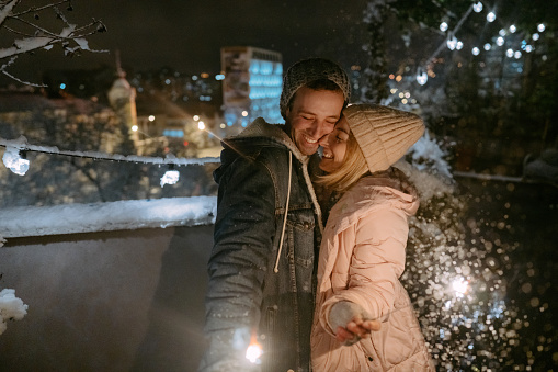 Photo of a young couple lighting sparklers and enjoying the beautiful snowy night together.