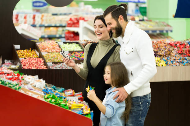 a young family with a little girl choose candy and chocolate in a large store, supermarket. - cake pick imagens e fotografias de stock