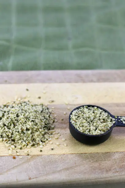 Wooden cutting board with a organic shelled hemp seeds also called hemp hearts in a pile and a measuring tablespoon. Shell-less organic hemp seed hearts on a cutting board in a pile and a tablespoon.