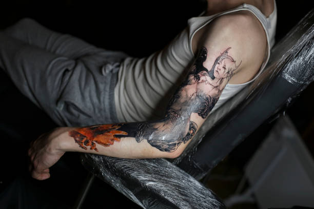 Young man with a tattoo Unrecognizable Caucasian young man getting a spooky horror tattoo on his arm. forearm tattoos men stock pictures, royalty-free photos & images