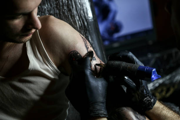Tattooing Unrecognizable Caucasian young man getting a spooky horror tattoo on his arm. forearm tattoos men stock pictures, royalty-free photos & images