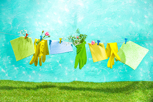 Creative bright spring cleaning concept. Tools, bottles, accessories for cleaning house with spring flowers and leaves hang on clothesline, box, bright sunny light copy space