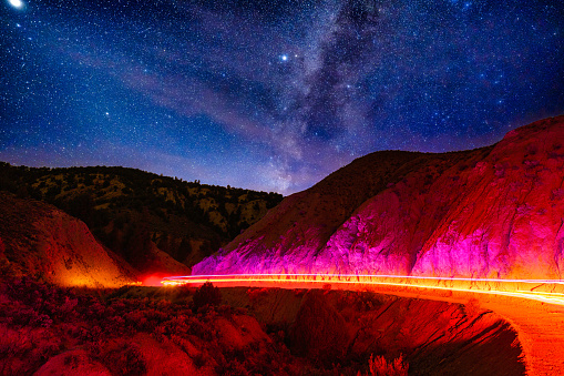 Dirt Road Through Canyon Night Astrophotography Light Trails - Scenic canyon with long time exposure of SUV vehicle driving and creating light trails around curves in dirt road.
