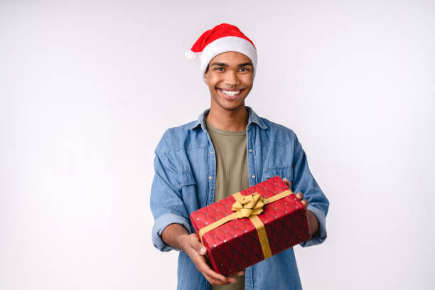 giovane uomo africano bello che consegna la scatola regalo regalo nel cappello di babbo natale per natale capodanno che si prepara per la festa invernale di celebrazione isolato su priorità bassa bianca - 12 18 months foto e immagini stock