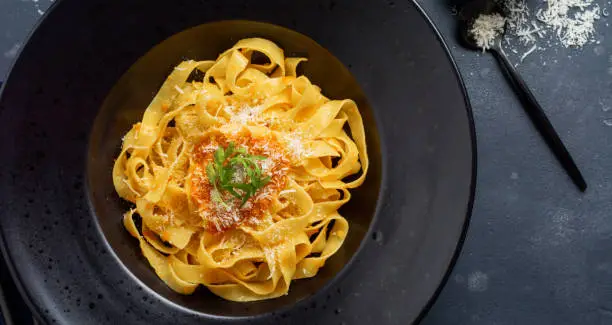 Fettuccine pasta with traditional Italian Passat sauce and parmesan cheese in black plate on dark background. Top view.