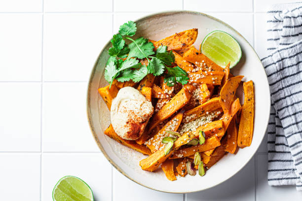 gajos de batata al horno con hummus, nueces y semillas en tazón. concepto de comida vegana saludable. - sweet potato french fries yam baked fotografías e imágenes de stock