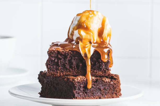 stack of brownie squares with scoop of ice cream and caramel, white background. - molho de sobremesa imagens e fotografias de stock