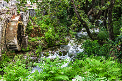 A mountain stream flows in the center of the Greek town of Livadia near the remains of an old watermill with a rusty wheel.
