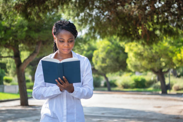 African young woman with t-shirt reading a book while standing in a park