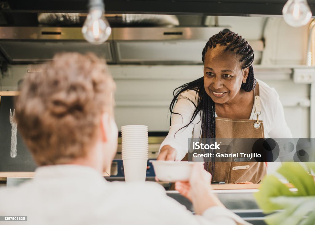 African chef woman serving take away order inside food truck - Focus on senior woman face Cafeteria Stock Photo