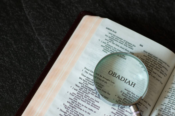 istock Open Holy Bible Book Old Testament Obadiah prophet with a magnifying glass on dark granite background 1357507017