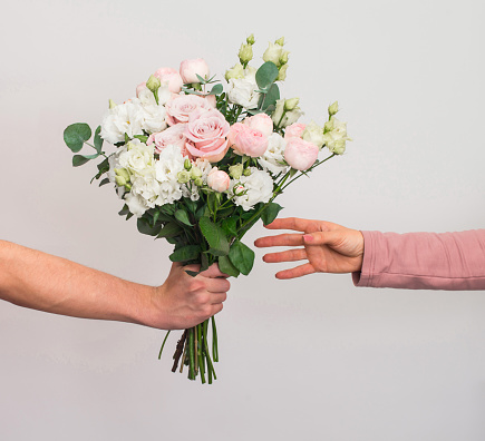 Concepto de entrega de flores. Mano dando ramo de flores pastel a la mujer sobre fondo gris. photo